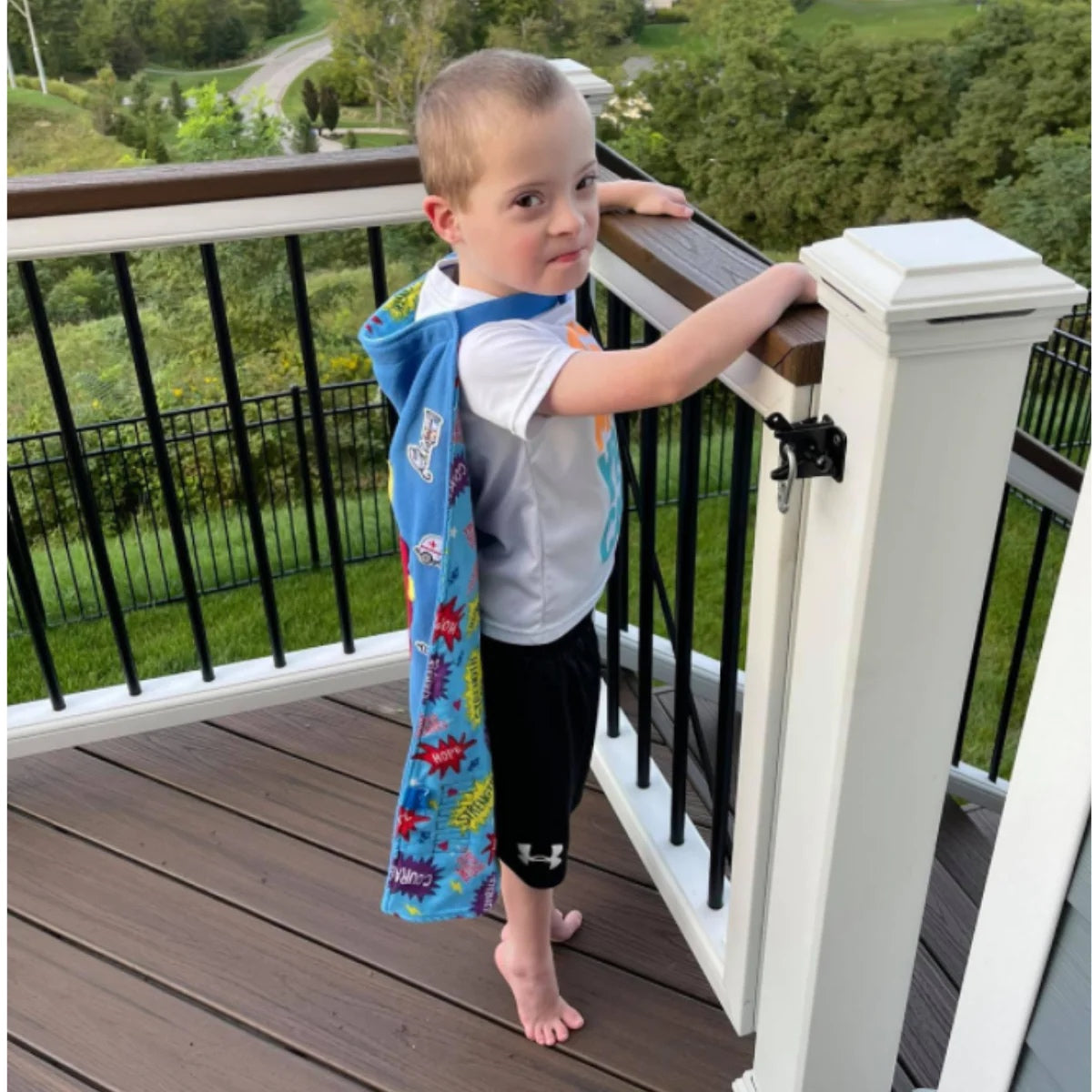 Boy on deck wearing his TinySuperheroes Cape and smling at camera