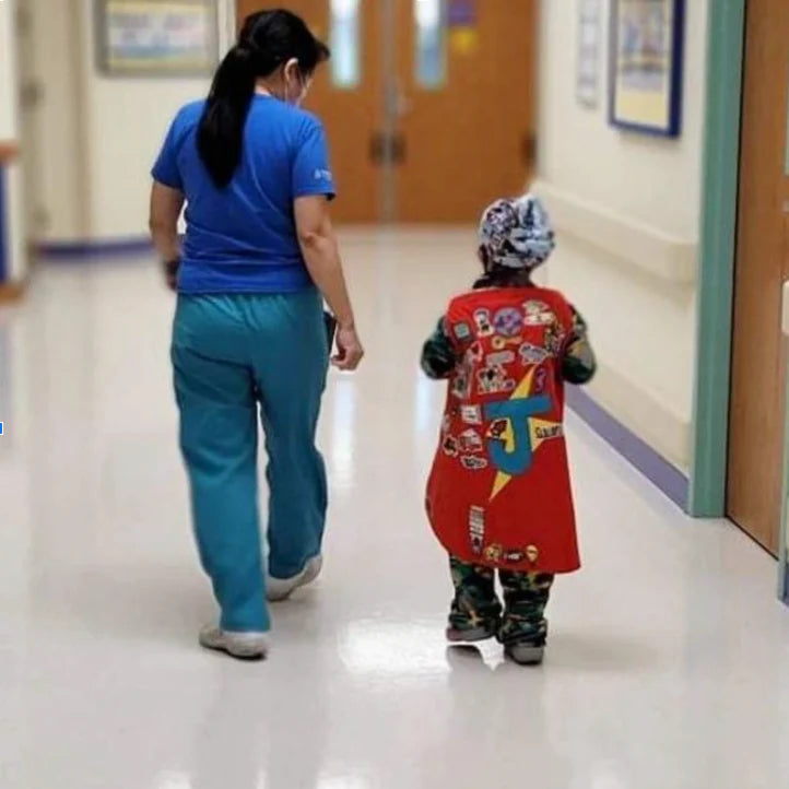 Photo of boy and nurse from behind walking down hospital hallway in his red TinySuperheroes Cape