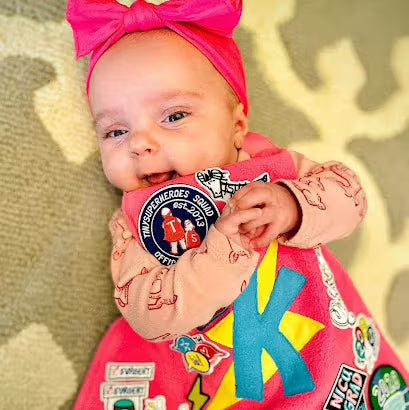 Photo of baby girl smiling and hugging her pink TinySupeheroes Cape